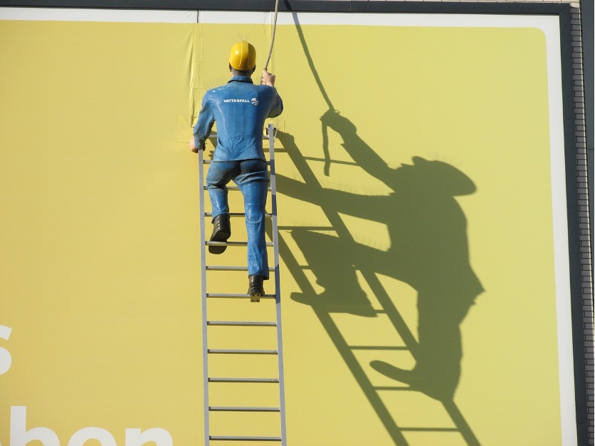 Man on a ladder up against a yellow wall